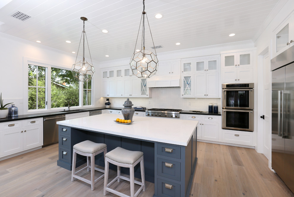 Inspiration for a transitional u-shaped medium tone wood floor kitchen remodel in Orange County with an undermount sink, white backsplash, subway tile backsplash, stainless steel appliances, an island, white cabinets and shaker cabinets