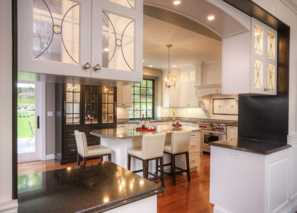 Inspiration for a large transitional medium tone wood floor eat-in kitchen remodel in Milwaukee with an undermount sink, raised-panel cabinets, white cabinets, quartz countertops, white backsplash, ceramic backsplash, stainless steel appliances and an island