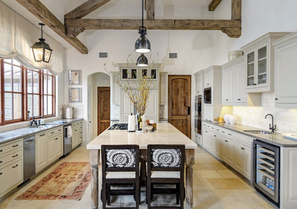 Example of a large tuscan u-shaped limestone floor and beige floor kitchen design in Austin with an undermount sink, white backsplash, subway tile backsplash, stainless steel appliances, an island, raised-panel cabinets, beige cabinets and gray countertops