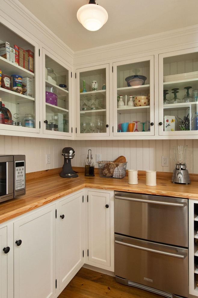 Klassisk inredning av ett kök, med träbänkskiva, luckor med glaspanel, vita skåp och rostfria vitvaror