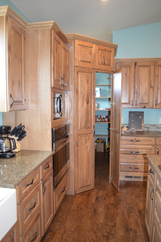 Lantlig inredning av ett kök, med en rustik diskho, luckor med upphöjd panel, skåp i ljust trä, bänkskiva i kvartsit, rostfria vitvaror, vinylgolv och en köksö