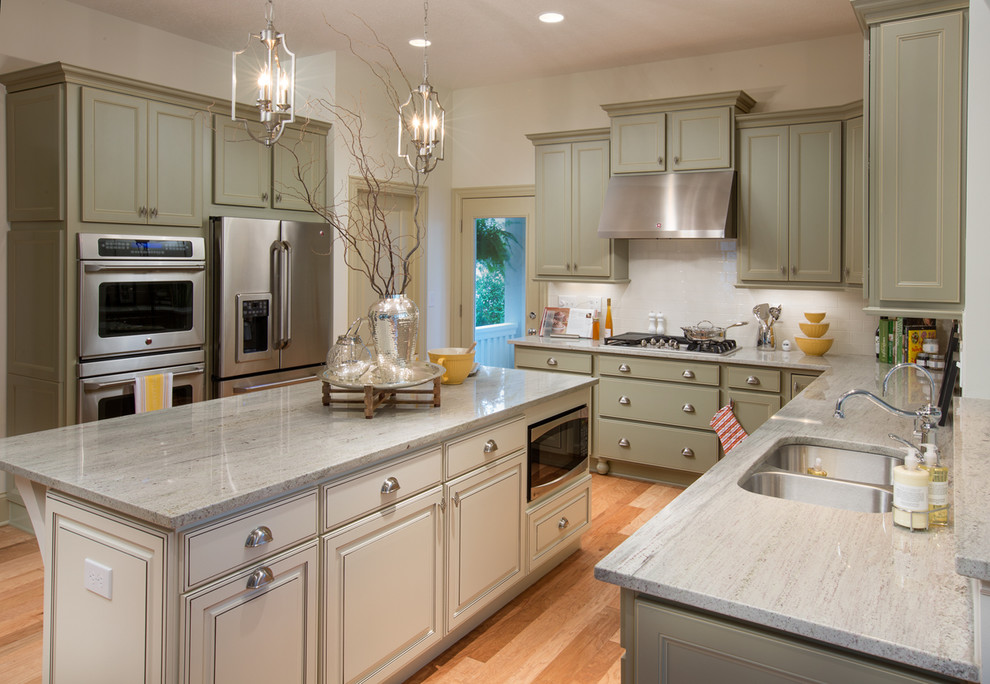 Inspiration for a mid-sized timeless l-shaped light wood floor open concept kitchen remodel in Columbus with a double-bowl sink, shaker cabinets, green cabinets, marble countertops, white backsplash, ceramic backsplash, stainless steel appliances and an island