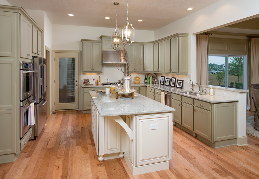 Mid-sized elegant l-shaped light wood floor open concept kitchen photo in Columbus with a double-bowl sink, shaker cabinets, green cabinets, marble countertops, white backsplash, ceramic backsplash, stainless steel appliances and an island