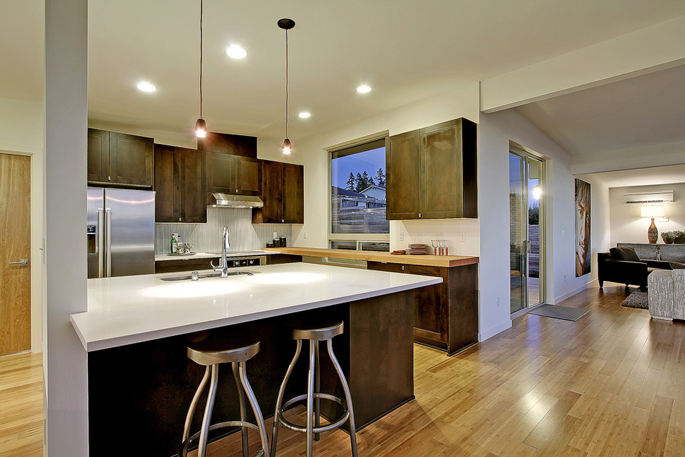 Offene Moderne Küche mit Schrankfronten mit vertiefter Füllung, dunklen Holzschränken, Küchenrückwand in Grau, Küchengeräten aus Edelstahl und weißer Arbeitsplatte in Seattle