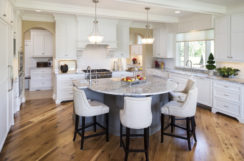 Inspiration for a timeless medium tone wood floor kitchen remodel in Minneapolis with an undermount sink, shaker cabinets, white cabinets, marble countertops, white backsplash, subway tile backsplash, stainless steel appliances and an island