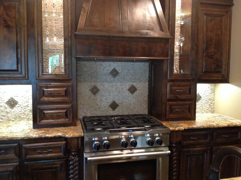 Immagine di un cucina con isola centrale rustico con ante con bugna sagomata, ante in legno bruno, top in granito, paraspruzzi grigio e elettrodomestici in acciaio inossidabile