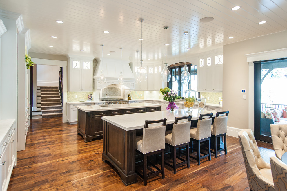 Inspiration for a large classic u-shaped kitchen/diner in Salt Lake City with shaker cabinets, white cabinets, multiple islands, a submerged sink, integrated appliances, engineered stone countertops, beige splashback, mosaic tiled splashback, medium hardwood flooring and brown floors.