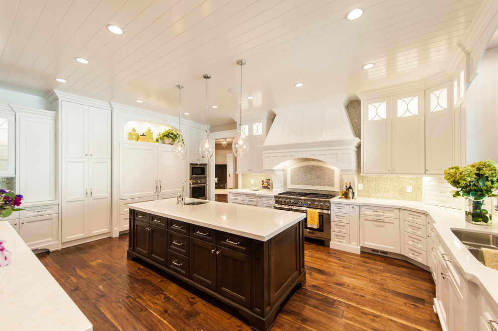 Photo of a large traditional u-shaped kitchen/diner in Salt Lake City with a submerged sink, shaker cabinets, white cabinets, engineered stone countertops, beige splashback, mosaic tiled splashback, integrated appliances, medium hardwood flooring, multiple islands and brown floors.