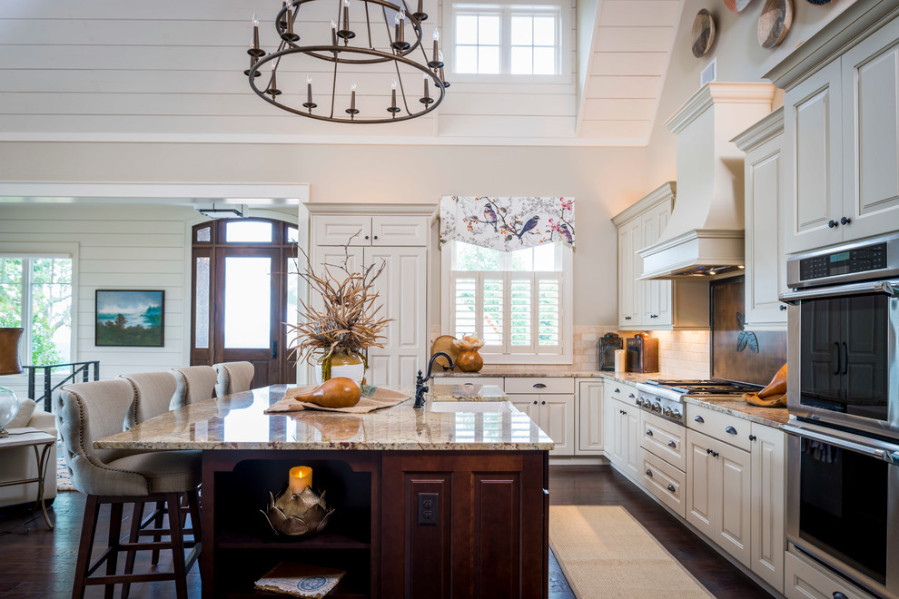Example of a mid-sized arts and crafts l-shaped dark wood floor open concept kitchen design in Other with a farmhouse sink, recessed-panel cabinets, distressed cabinets, granite countertops, beige backsplash, stone tile backsplash, paneled appliances and an island