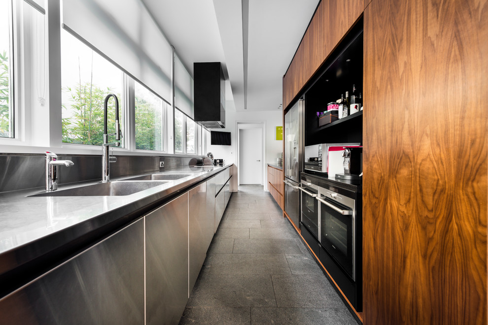 Exemple d'une cuisine parallèle moderne en bois brun fermée avec un évier 2 bacs, un placard à porte plane, un plan de travail en inox, une crédence grise et un électroménager en acier inoxydable.