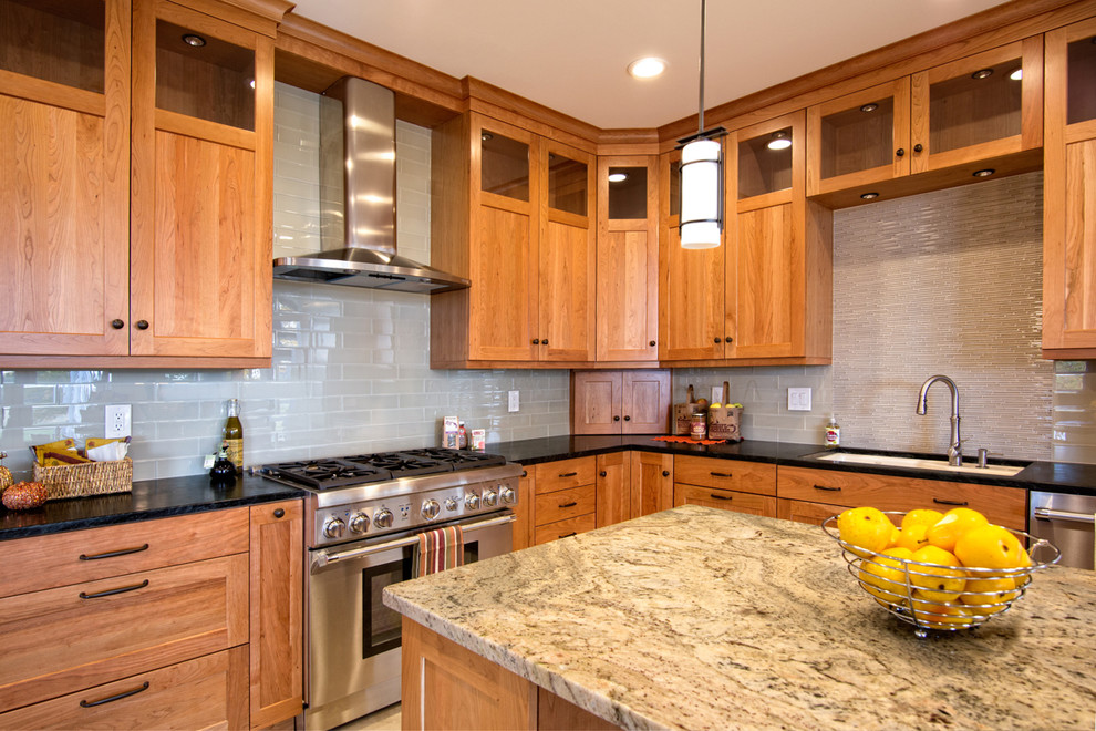 Example of an arts and crafts ceramic tile kitchen design in Bridgeport with a drop-in sink, shaker cabinets, medium tone wood cabinets, soapstone countertops, beige backsplash, glass tile backsplash, stainless steel appliances and an island