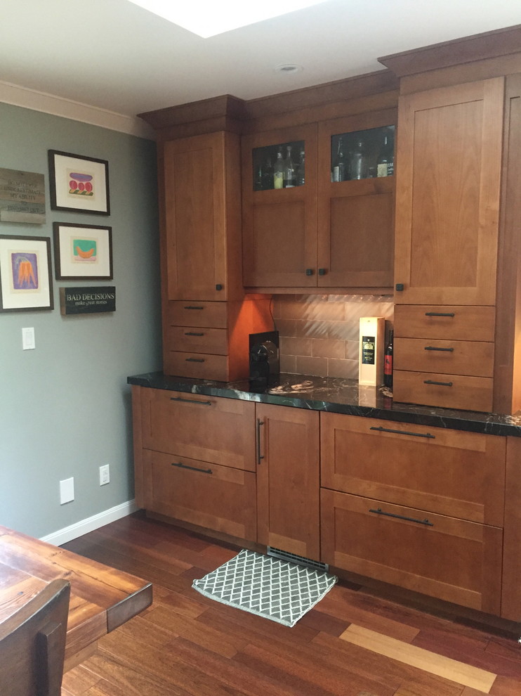 Example of a large arts and crafts dark wood floor eat-in kitchen design in Other with a farmhouse sink, shaker cabinets, brown cabinets, granite countertops, gray backsplash, glass tile backsplash, paneled appliances and an island