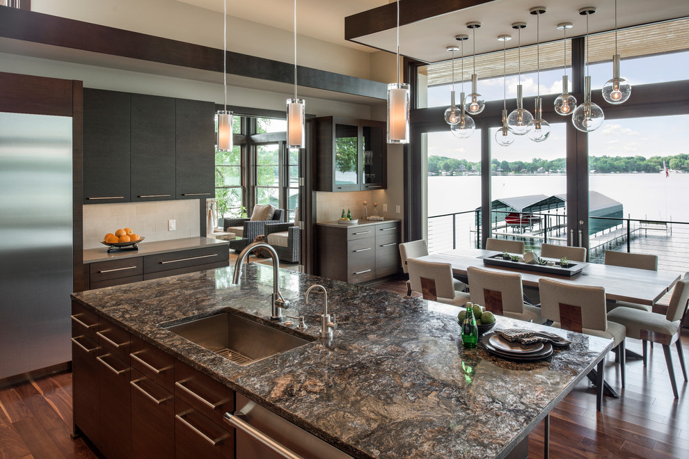 Open concept kitchen - huge contemporary l-shaped medium tone wood floor open concept kitchen idea in Minneapolis with an undermount sink, flat-panel cabinets, dark wood cabinets, granite countertops, beige backsplash, stone tile backsplash, stainless steel appliances and an island
