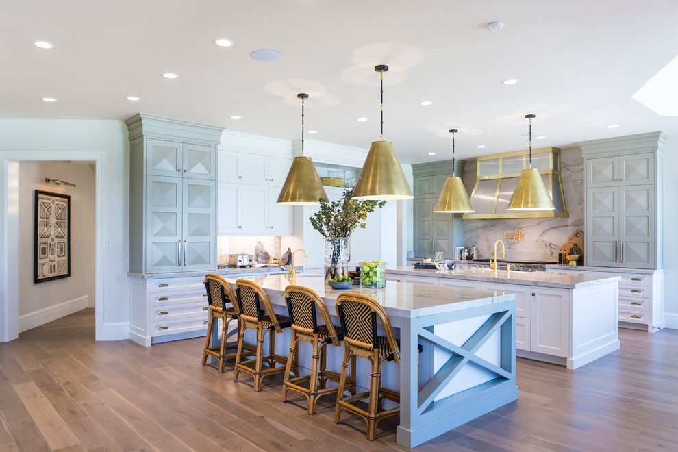 This is an example of an expansive classic l-shaped kitchen in Salt Lake City with shaker cabinets, white cabinets, white splashback, medium hardwood flooring, multiple islands, brown floors, a belfast sink, stone slab splashback, integrated appliances and quartz worktops.