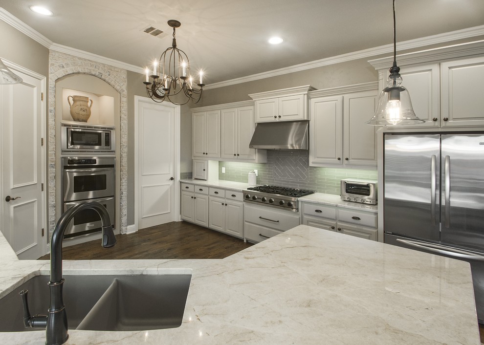 Example of a mid-sized classic u-shaped dark wood floor open concept kitchen design in Dallas with an undermount sink, raised-panel cabinets, white cabinets, gray backsplash, stainless steel appliances and a peninsula