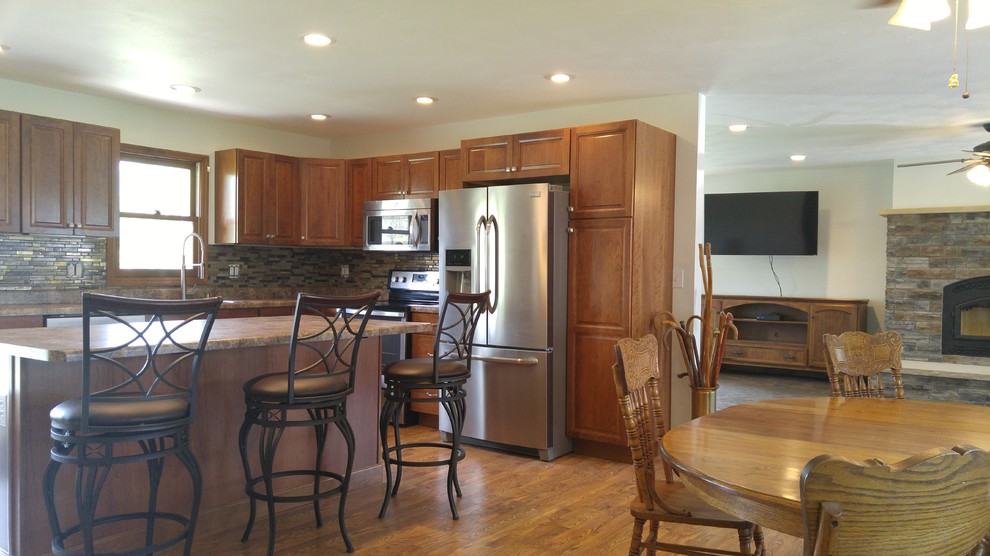 Large farmhouse l-shaped kitchen/diner in Indianapolis with a built-in sink, raised-panel cabinets, medium wood cabinets, laminate countertops, brown splashback, glass tiled splashback, stainless steel appliances, medium hardwood flooring and an island.