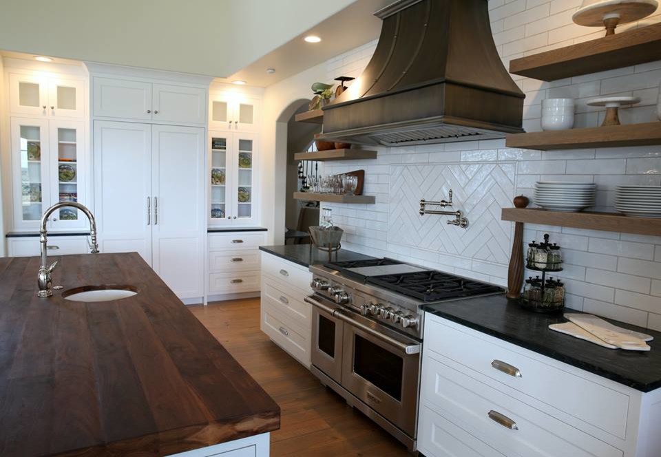 Inspiration for a mid-sized shabby-chic style u-shaped medium tone wood floor and beige floor eat-in kitchen remodel in Orange County with a drop-in sink, raised-panel cabinets, white cabinets, wood countertops, brown backsplash, subway tile backsplash, stainless steel appliances and two islands