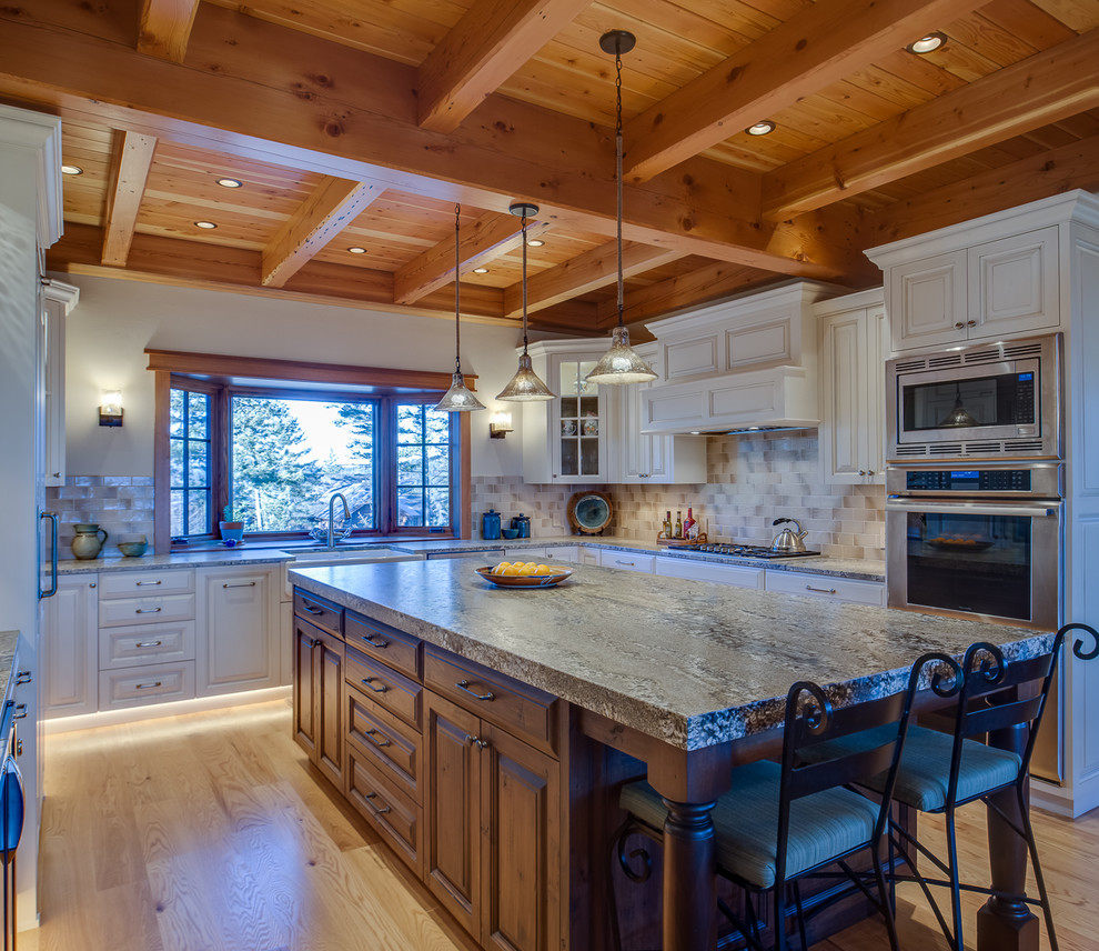 Exempel på ett avskilt, stort rustikt u-kök, med en rustik diskho, luckor med upphöjd panel, vita skåp, granitbänkskiva, beige stänkskydd, stänkskydd i stenkakel, rostfria vitvaror, ljust trägolv och en köksö