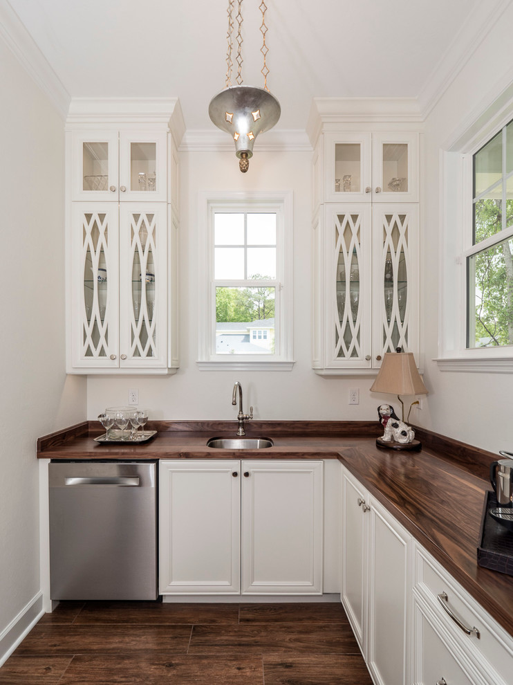 Klassisk inredning av ett kök, med en undermonterad diskho, luckor med glaspanel, vita skåp, träbänkskiva, rostfria vitvaror och klinkergolv i porslin