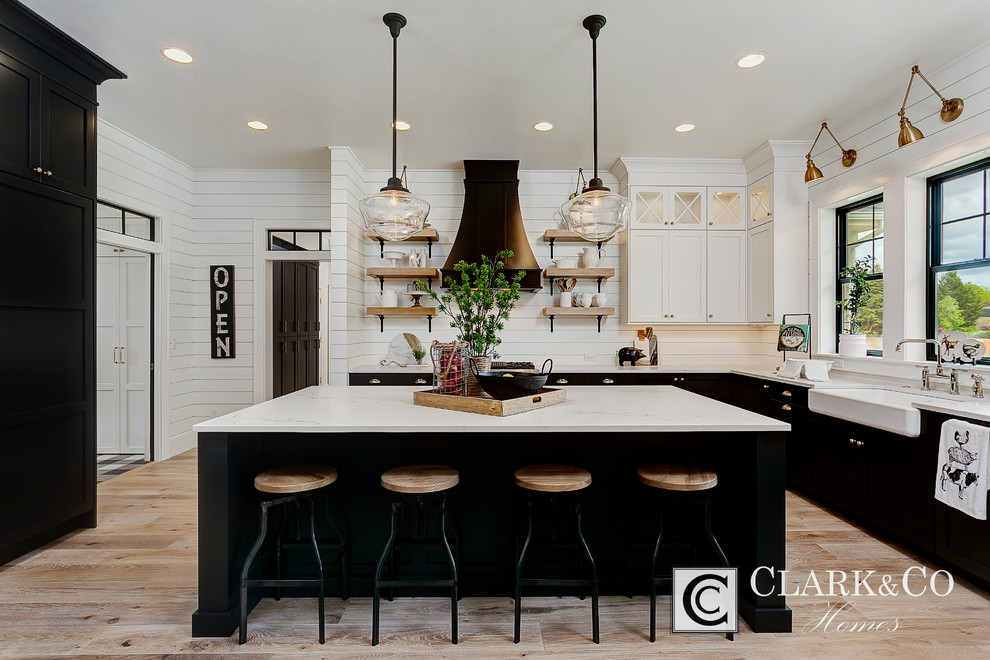 Example of a large farmhouse u-shaped light wood floor open concept kitchen design in Boise with a farmhouse sink, shaker cabinets, white cabinets, quartz countertops, white backsplash, wood backsplash, stainless steel appliances and an island