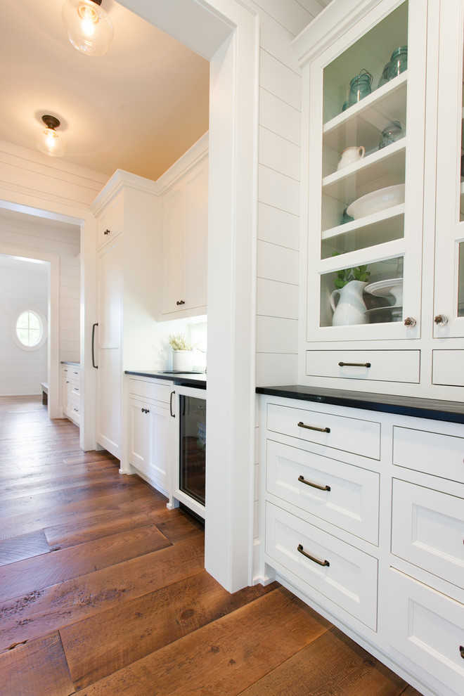 Example of an eclectic galley medium tone wood floor and brown floor kitchen pantry design with a drop-in sink, white cabinets, granite countertops and white backsplash
