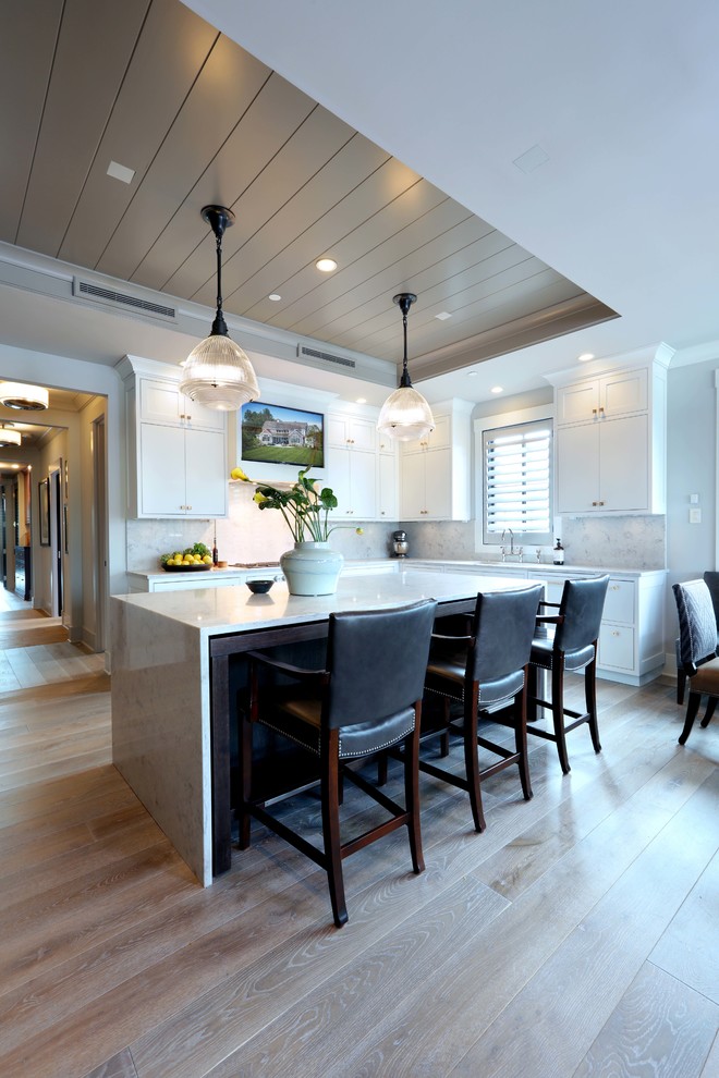 Cette photo montre une cuisine ouverte parallèle moderne de taille moyenne avec un évier posé, des portes de placard blanches, une crédence blanche, parquet clair, îlot et un sol marron.
