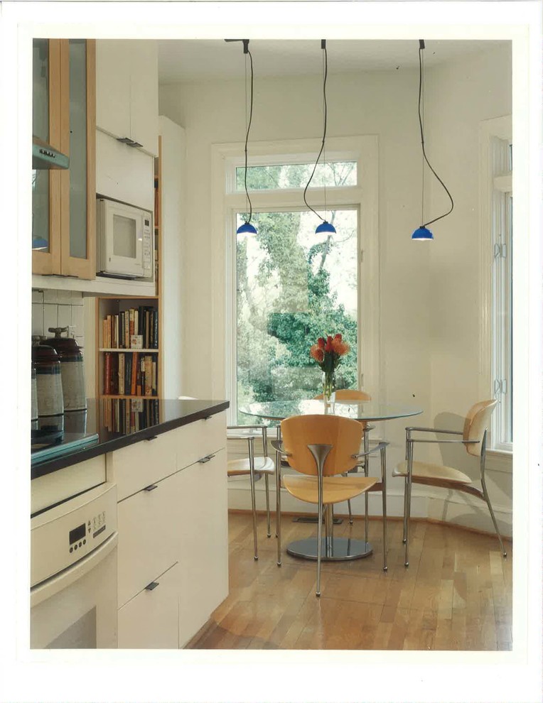 Пример оригинального дизайна: параллельная кухня в стиле фьюжн с обеденным столом, плоскими фасадами, белыми фасадами, белым фартуком, белой техникой, светлым паркетным полом и коричневым полом