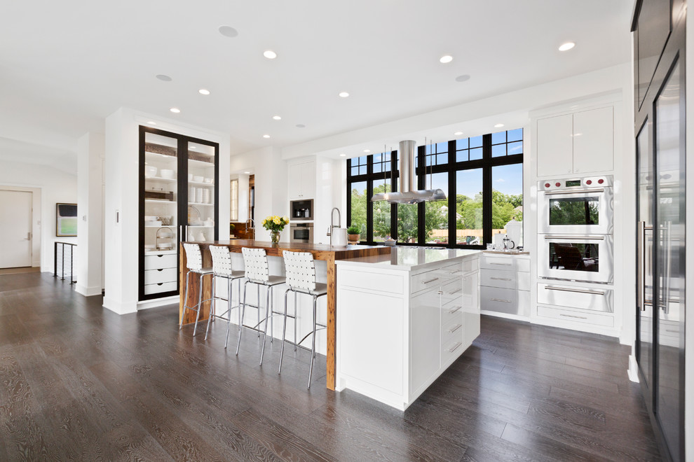 Inspiration for a large contemporary u-shaped medium tone wood floor and brown floor eat-in kitchen remodel in Minneapolis with a farmhouse sink, flat-panel cabinets, white cabinets, wood countertops, stainless steel appliances, an island and brown countertops