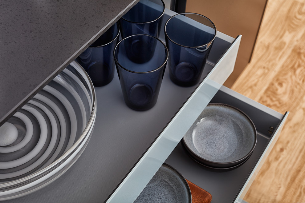Foto di un'ampia cucina minimalista con lavello sottopiano, ante lisce, ante nere, top in superficie solida, elettrodomestici neri e parquet chiaro