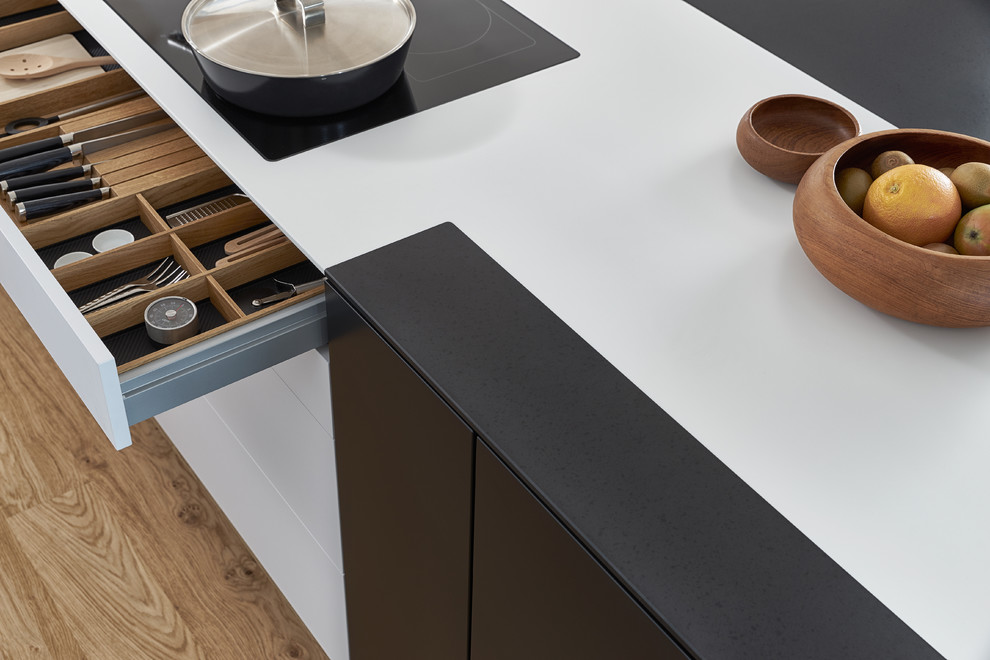 Esempio di un'ampia cucina moderna con lavello sottopiano, ante lisce, ante nere, top in superficie solida, elettrodomestici neri e parquet chiaro