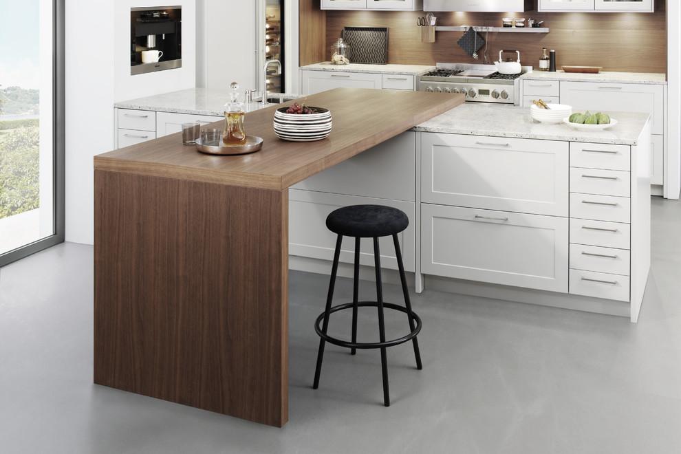 Design ideas for a large modern l-shaped kitchen/diner in New York with shaker cabinets, white cabinets, laminate countertops, brown splashback, stainless steel appliances, concrete flooring, a breakfast bar and a belfast sink.