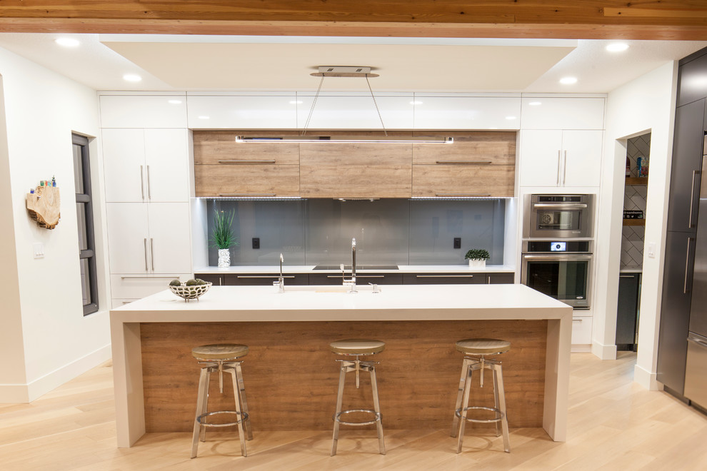 Large trendy galley light wood floor eat-in kitchen photo in Edmonton with an undermount sink, flat-panel cabinets, white cabinets, solid surface countertops, gray backsplash, glass sheet backsplash, stainless steel appliances and an island