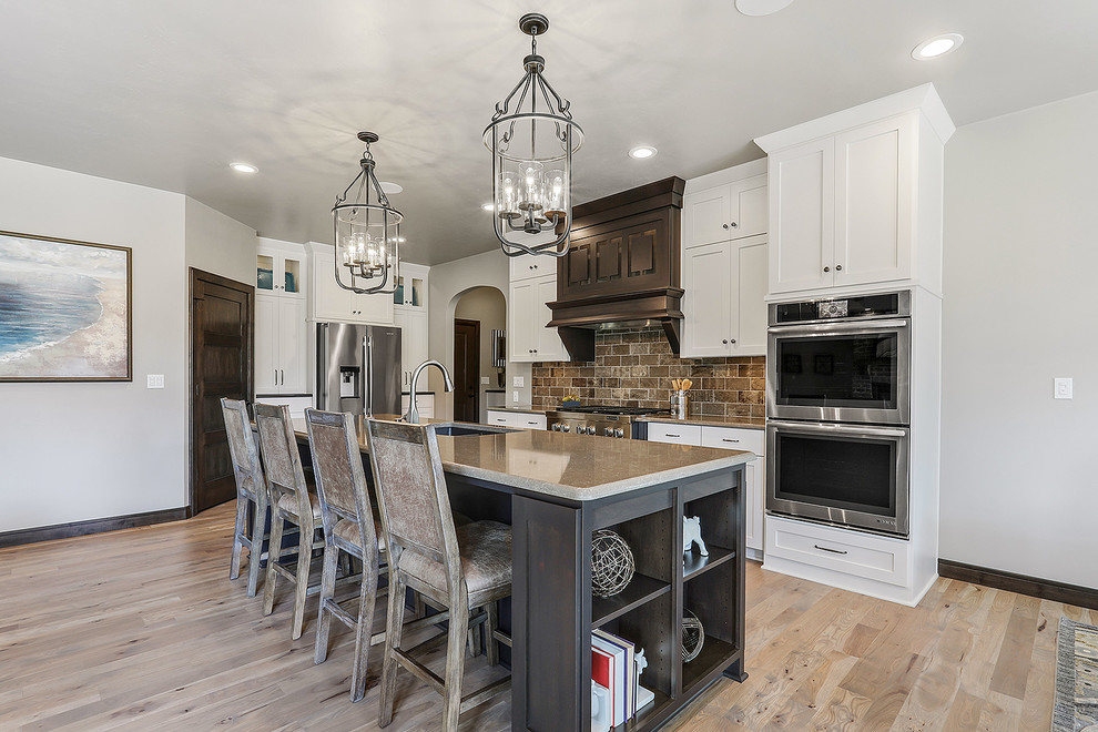 Mid-sized arts and crafts single-wall light wood floor and beige floor open concept kitchen photo with an undermount sink, shaker cabinets, white cabinets, quartz countertops, brown backsplash, subway tile backsplash, stainless steel appliances and an island