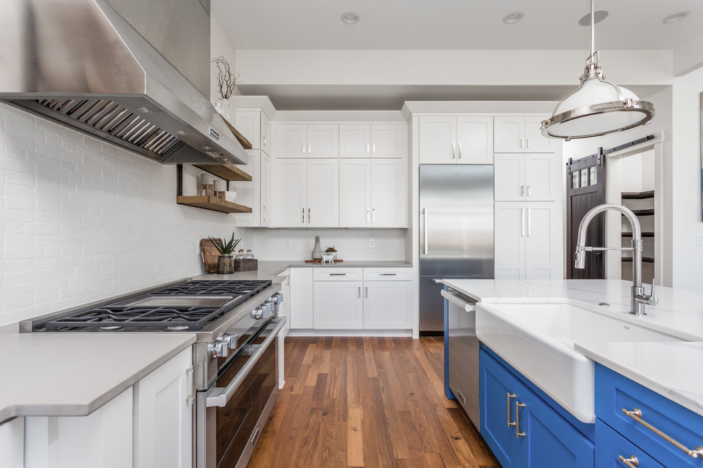 Bild på ett stort lantligt kök, med en rustik diskho, skåp i shakerstil, vita skåp, vitt stänkskydd, stänkskydd i tegel, rostfria vitvaror, mellanmörkt trägolv, en köksö och flerfärgat golv