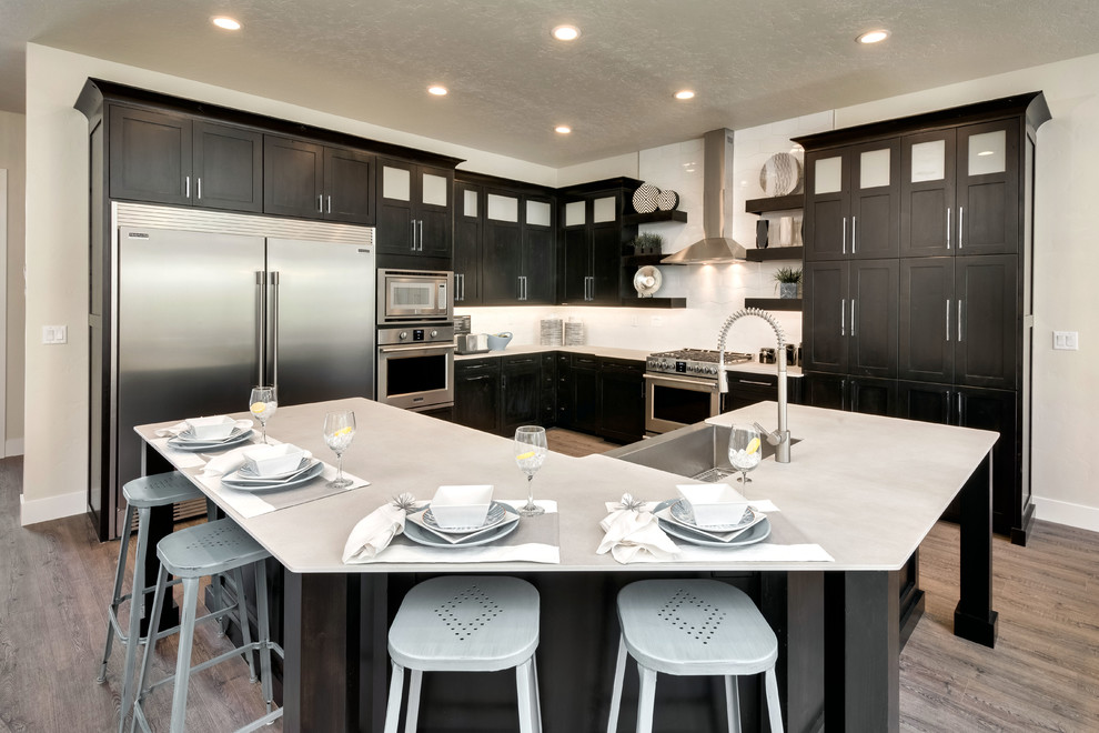 Open concept kitchen - mid-sized modern l-shaped light wood floor and multicolored floor open concept kitchen idea in Boise with a farmhouse sink, shaker cabinets, black cabinets, concrete countertops, white backsplash, porcelain backsplash, stainless steel appliances and an island