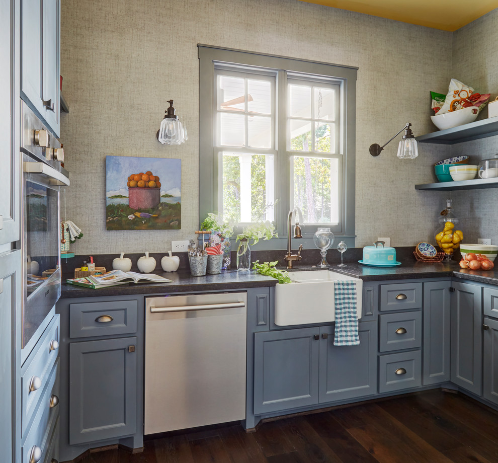 Klassisk inredning av ett litet u-kök, med en rustik diskho, skåp i shakerstil, blå skåp, fönster som stänkskydd, rostfria vitvaror, mörkt trägolv och brunt golv