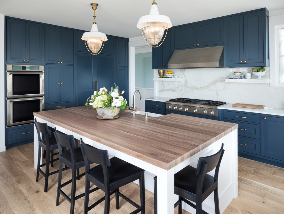 Inspiration for a coastal light wood floor and beige floor kitchen remodel in Minneapolis with a farmhouse sink, shaker cabinets, blue cabinets, white backsplash, marble backsplash, stainless steel appliances, an island and white countertops