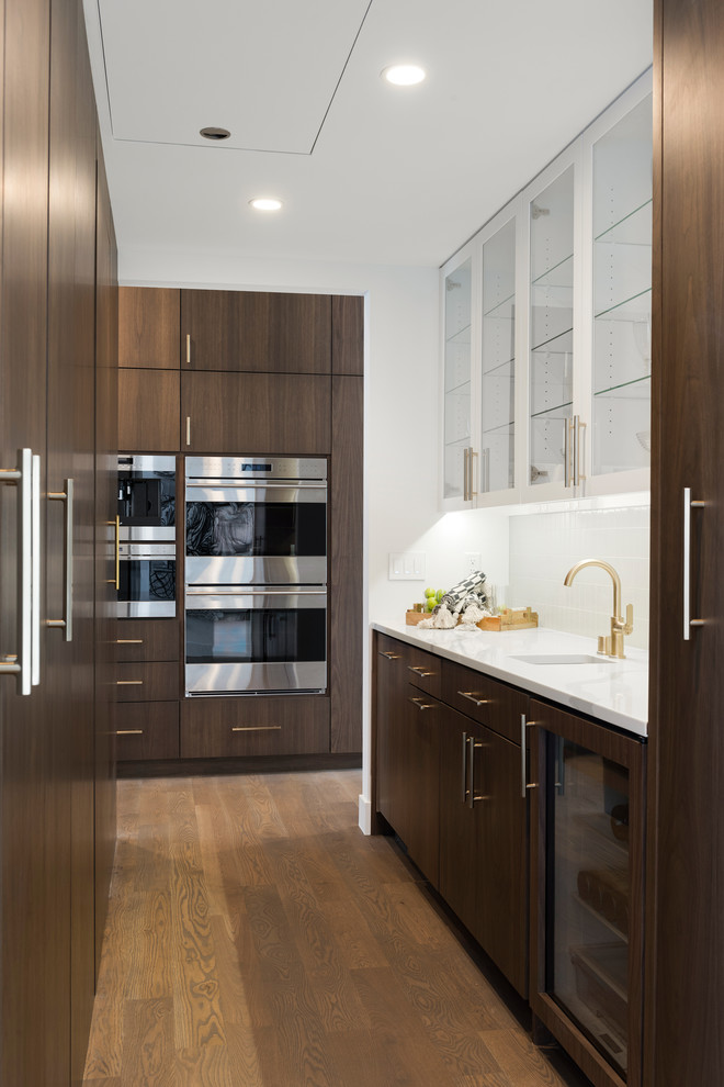 Design ideas for a large modern galley kitchen pantry in Minneapolis with a submerged sink, flat-panel cabinets, medium wood cabinets, engineered stone countertops, white splashback, ceramic splashback, integrated appliances, light hardwood flooring, an island, grey floors and white worktops.