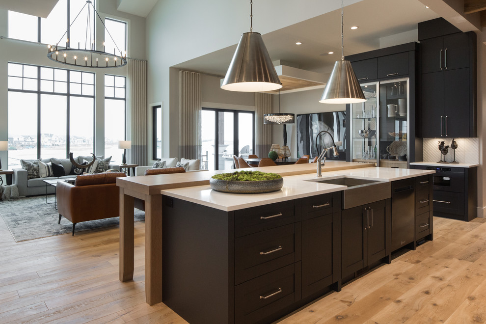 Inspiration for a huge country single-wall medium tone wood floor and brown floor open concept kitchen remodel in Calgary with an undermount sink, shaker cabinets, black cabinets, quartz countertops, white backsplash, ceramic backsplash, black appliances, an island and white countertops