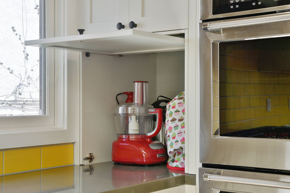 Exempel på ett mellanstort, avskilt klassiskt grå grått u-kök, med en undermonterad diskho, skåp i shakerstil, vita skåp, bänkskiva i kvarts, gult stänkskydd, stänkskydd i keramik, rostfria vitvaror, mellanmörkt trägolv, en halv köksö och brunt golv