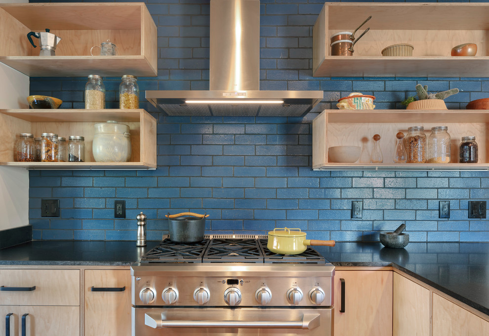 Idéer för att renovera ett mellanstort funkis svart svart kök, med släta luckor, skåp i ljust trä, granitbänkskiva, blått stänkskydd, stänkskydd i keramik, rostfria vitvaror, mellanmörkt trägolv, en halv köksö och brunt golv