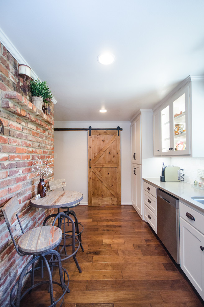 Inspiration for a medium sized rustic single-wall enclosed kitchen in Dallas with a built-in sink, shaker cabinets, white cabinets, white splashback, stone tiled splashback, stainless steel appliances, medium hardwood flooring, no island, brown floors and white worktops.