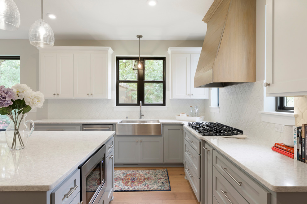 Large trendy u-shaped medium tone wood floor and brown floor open concept kitchen photo in Minneapolis with a farmhouse sink, flat-panel cabinets, gray cabinets, quartz countertops, white backsplash, ceramic backsplash, stainless steel appliances, an island and white countertops