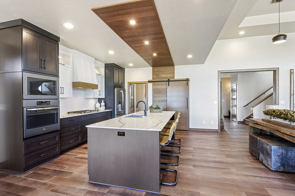 Foto på ett mellanstort funkis vit kök med öppen planlösning, med en undermonterad diskho, släta luckor, bänkskiva i kvartsit, vitt stänkskydd, stänkskydd i keramik, rostfria vitvaror, mellanmörkt trägolv, en köksö och brunt golv
