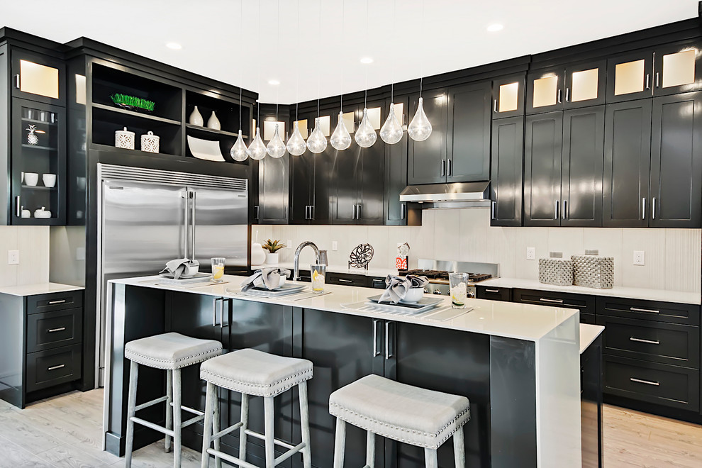 Mittelgroße Moderne Küche in L-Form mit Schrankfronten im Shaker-Stil, schwarzen Schränken, Küchenrückwand in Weiß, Küchengeräten aus Edelstahl, hellem Holzboden, Kücheninsel, beigem Boden und weißer Arbeitsplatte in Boise