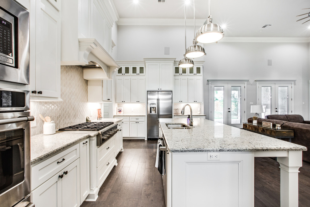 Example of a transitional l-shaped dark wood floor and brown floor open concept kitchen design in Austin with a double-bowl sink, recessed-panel cabinets, white cabinets, beige backsplash, stainless steel appliances, an island and gray countertops
