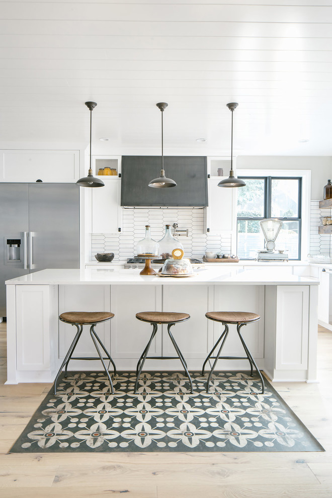 Farmhouse l-shaped kitchen/diner in Seattle with shaker cabinets, white cabinets, white splashback, stainless steel appliances, light hardwood flooring, an island, beige floors and white worktops.