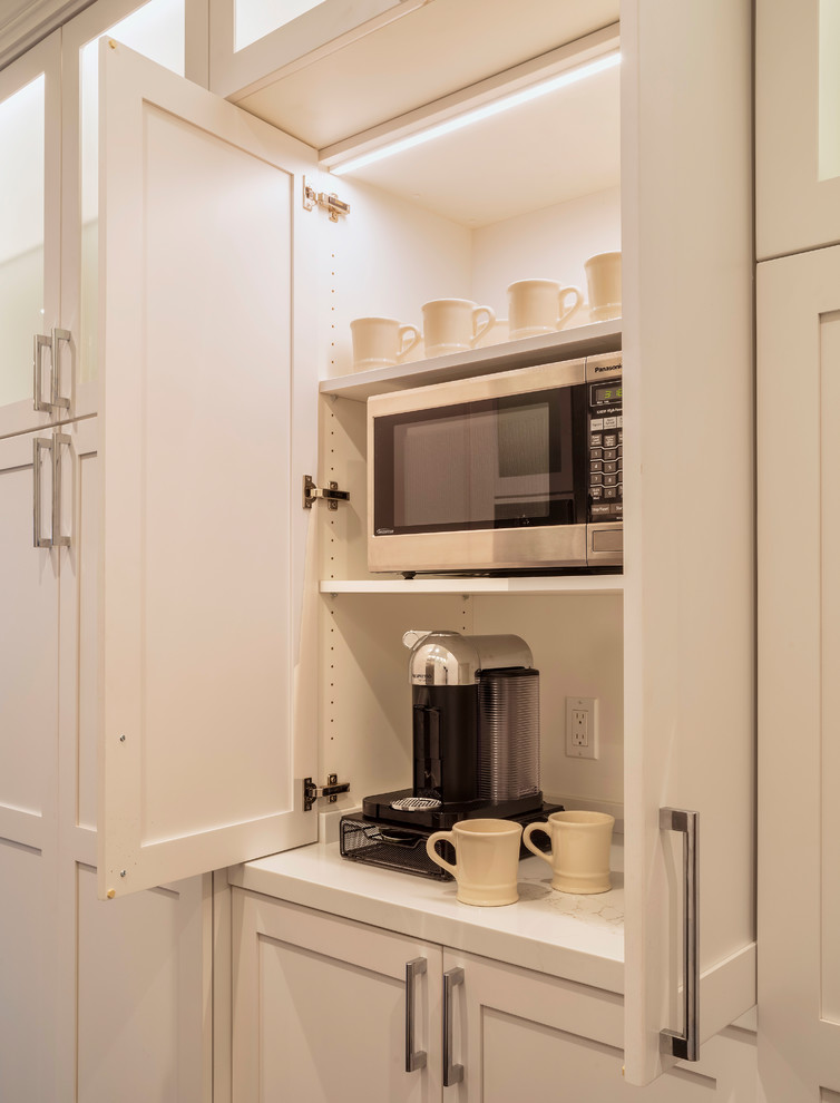 Inredning av ett klassiskt stort vit vitt kök, med en undermonterad diskho, skåp i shakerstil, vita skåp, bänkskiva i kvarts, vitt stänkskydd, stänkskydd i tunnelbanekakel, rostfria vitvaror, mörkt trägolv, en halv köksö och brunt golv