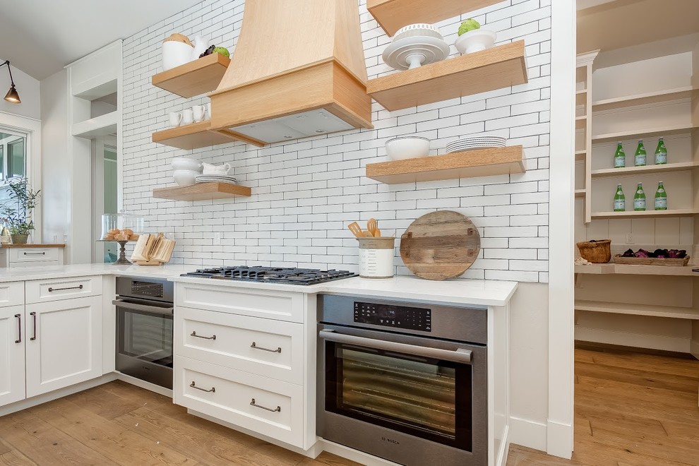 Modern inredning av ett stort vit vitt kök, med en rustik diskho, luckor med infälld panel, vita skåp, bänkskiva i koppar, vitt stänkskydd, stänkskydd i tunnelbanekakel, rostfria vitvaror, mellanmörkt trägolv, en köksö och brunt golv
