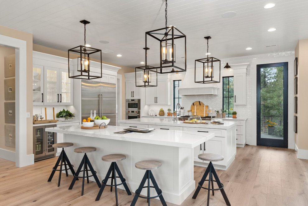 Design ideas for a classic kitchen in Denver with shaker cabinets, white cabinets, white splashback, stainless steel appliances, light hardwood flooring, multiple islands, brown floors and white worktops.
